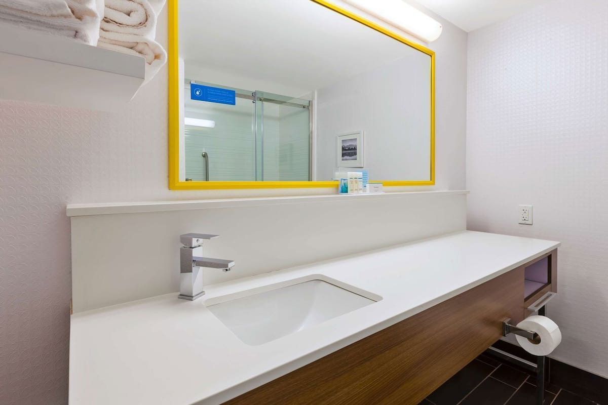 Un baño moderno con un lavabo blanco, un espejo con marco amarillo y un toallero sobre el lavabo.
