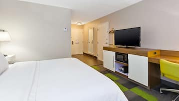 Quarto de hotel com uma cama, uma mesa com televisão, uma cadeira e um abajur.