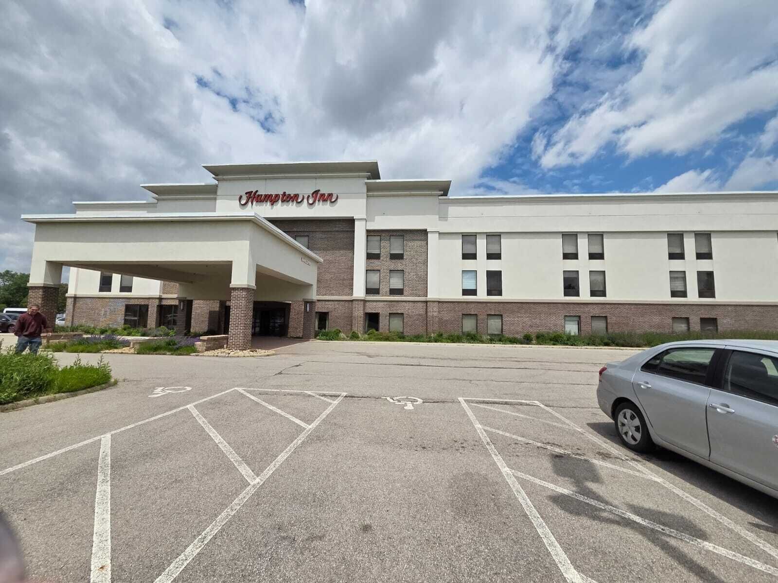 A Hampton Inn hotel with a covered entrance, parking lot, and a clear sky.