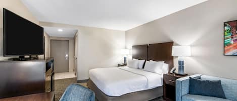 A hotel room with a bed, a television, a desk, a chair, a sofa, and a painting on the wall.