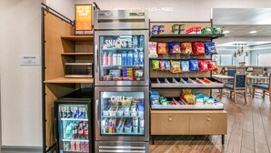 A snack and drink vending area with a microwave and a sign indicating a treats shop. - Hampton Inn Milledgeville (Milledgeville)