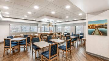 A spacious dining area with multiple tables and chairs, large windows, and a view of a landscape painting.