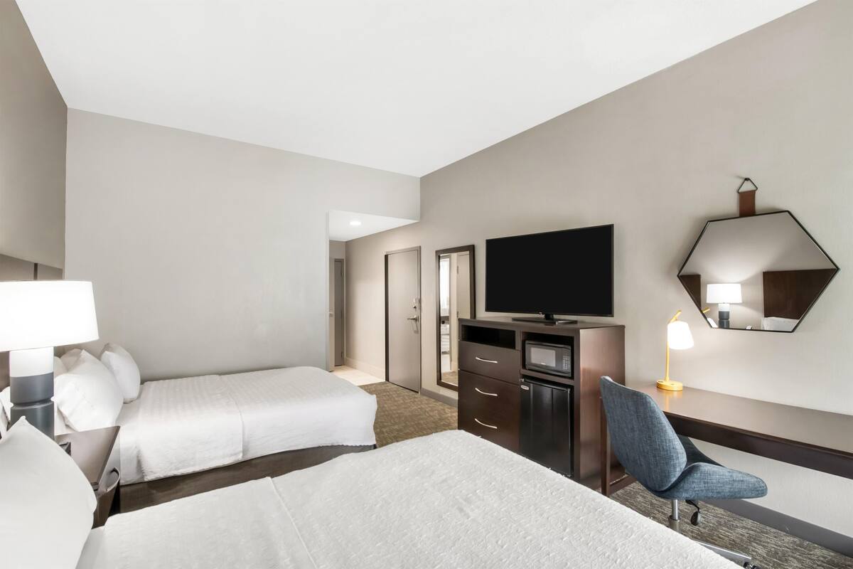Een hotelkamer met twee bedden, een televisie, een bureau met stoel, een lamp en een spiegel.