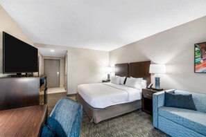 A hotel room with a bed, a TV, a desk, a chair, a sofa, and a painting on the wall. - Hampton Inn Milledgeville (Milledgeville)