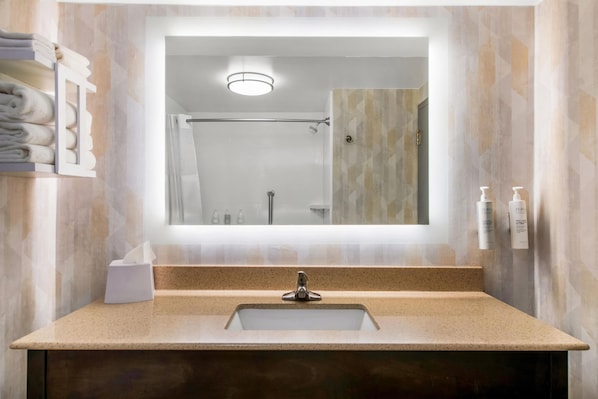 Un baño con lavamanos, espejo, toallero y ducha.