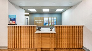 A reception desk with a wooden panel design, a 'Welcome to Hampton' sign, and a Hilton Honors sign. - Hampton Inn Milledgeville (Milledgeville)