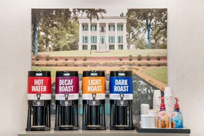 Estación de café con cuatro dispensadores etiquetados como 'Agua Caliente', 'Café Descafeinado', 'Tueste Suave' y 'Tueste Oscuro'.