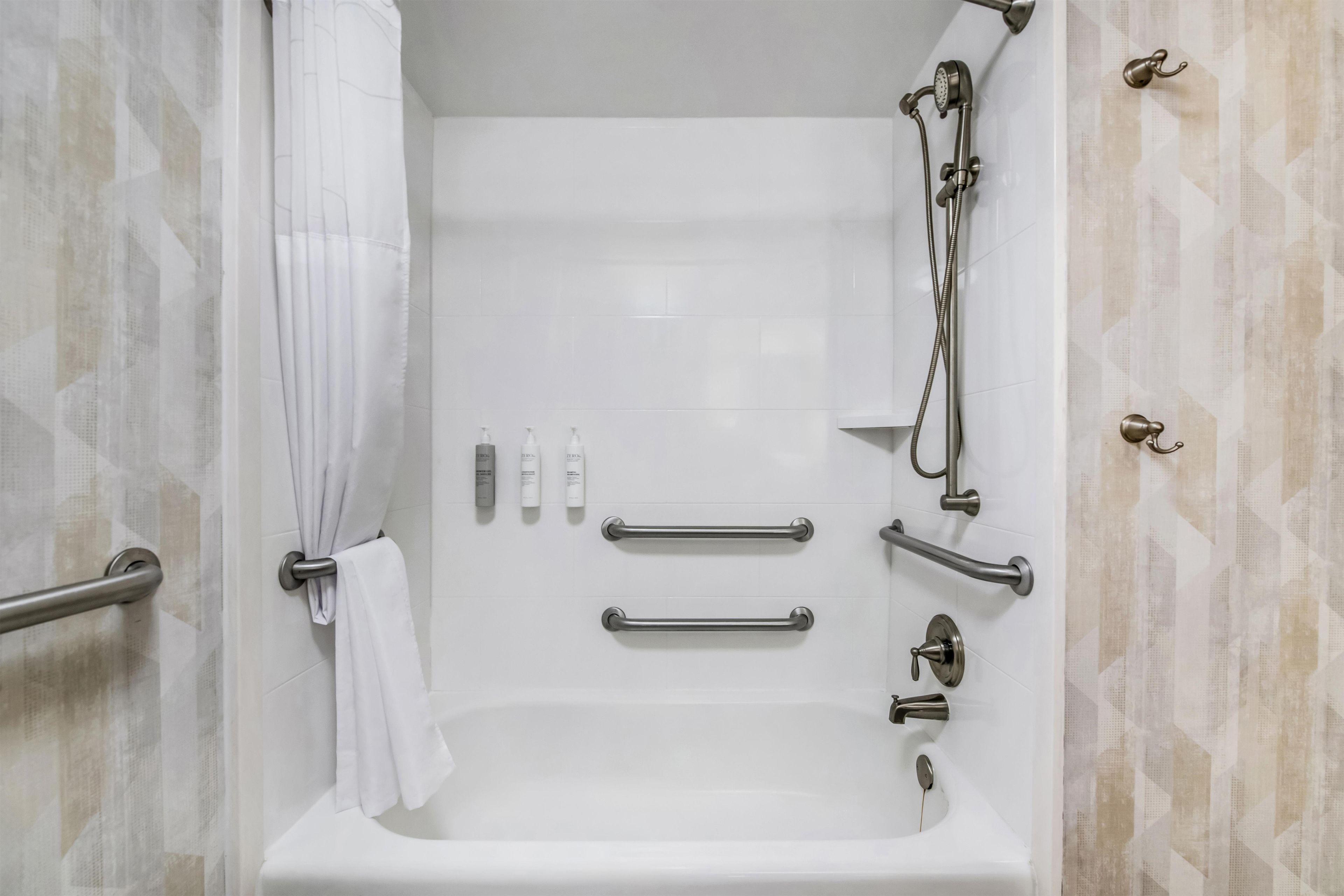 A white bathtub with grab bars, a showerhead, and a towel rack.
