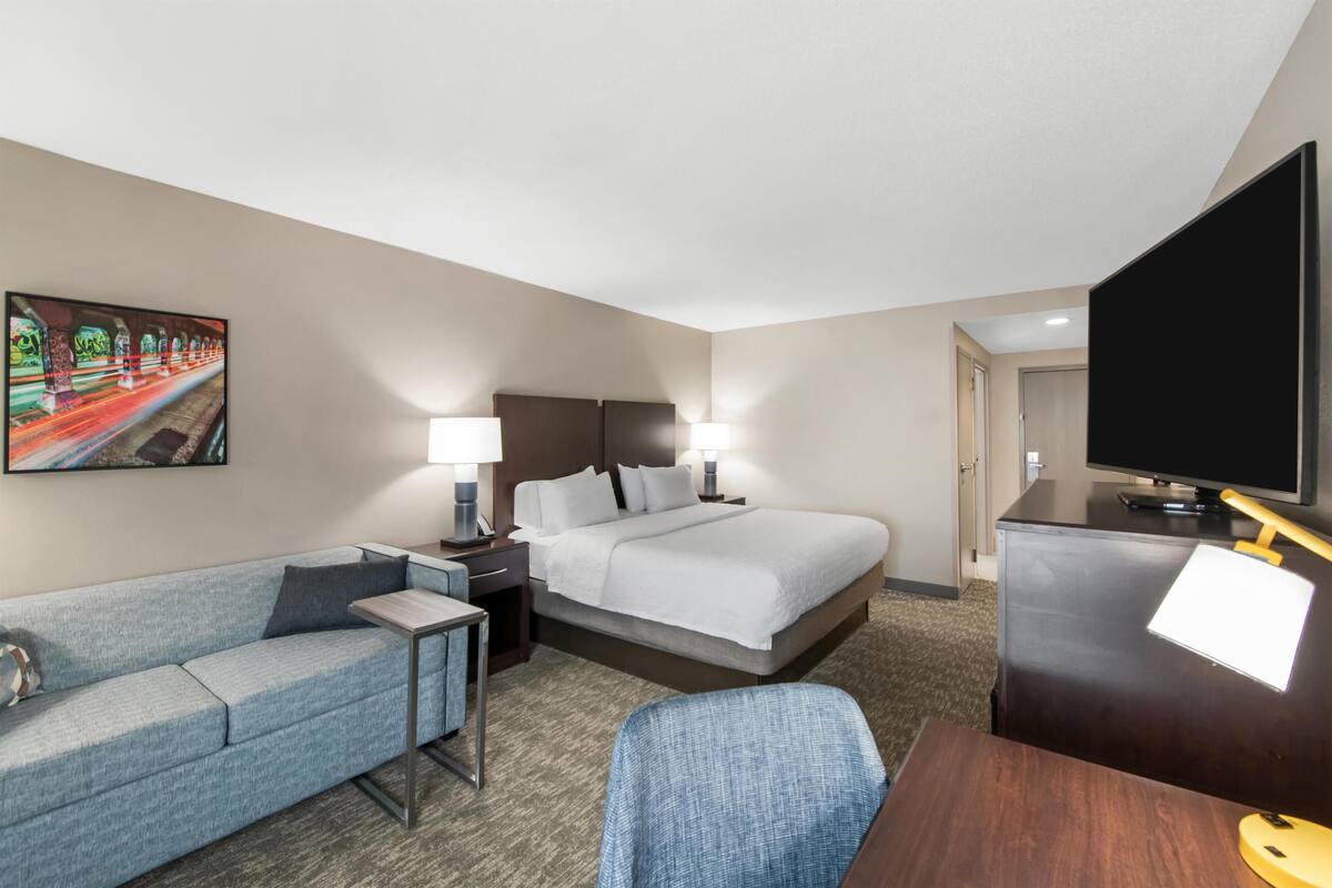 Een hotelkamer met een bed, een slaapbank, een bureau, een televisie en een schilderij aan de muur.