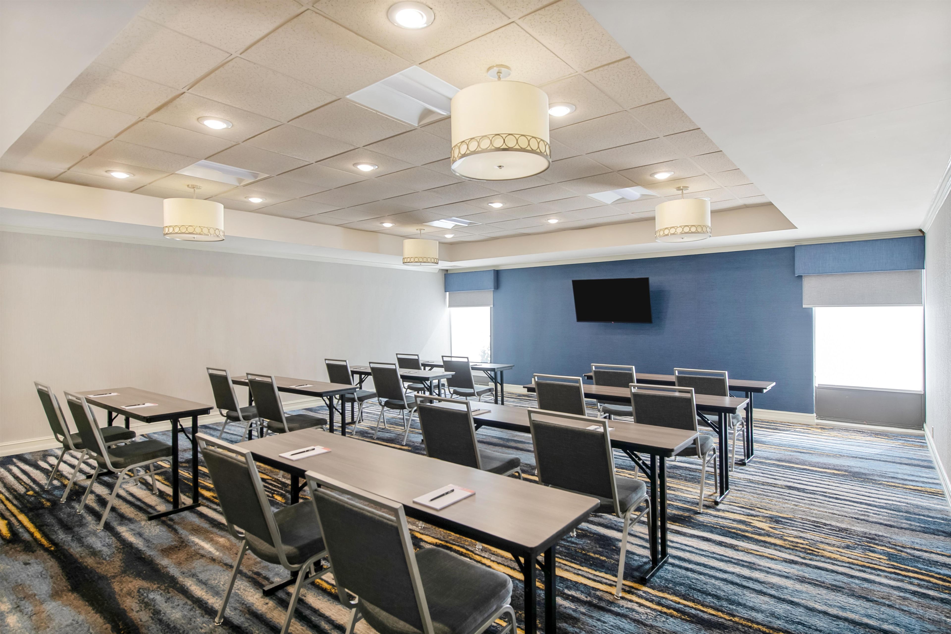 A conference room with multiple tables and chairs, a flat-screen TV on the wall, and ceiling lights.