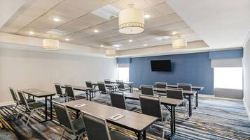 A conference room with multiple tables and chairs, a flat-screen TV on the wall, and ceiling lights.