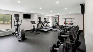 Un gimnasio con máquinas de cardio, bancos de pesas y un espejo.