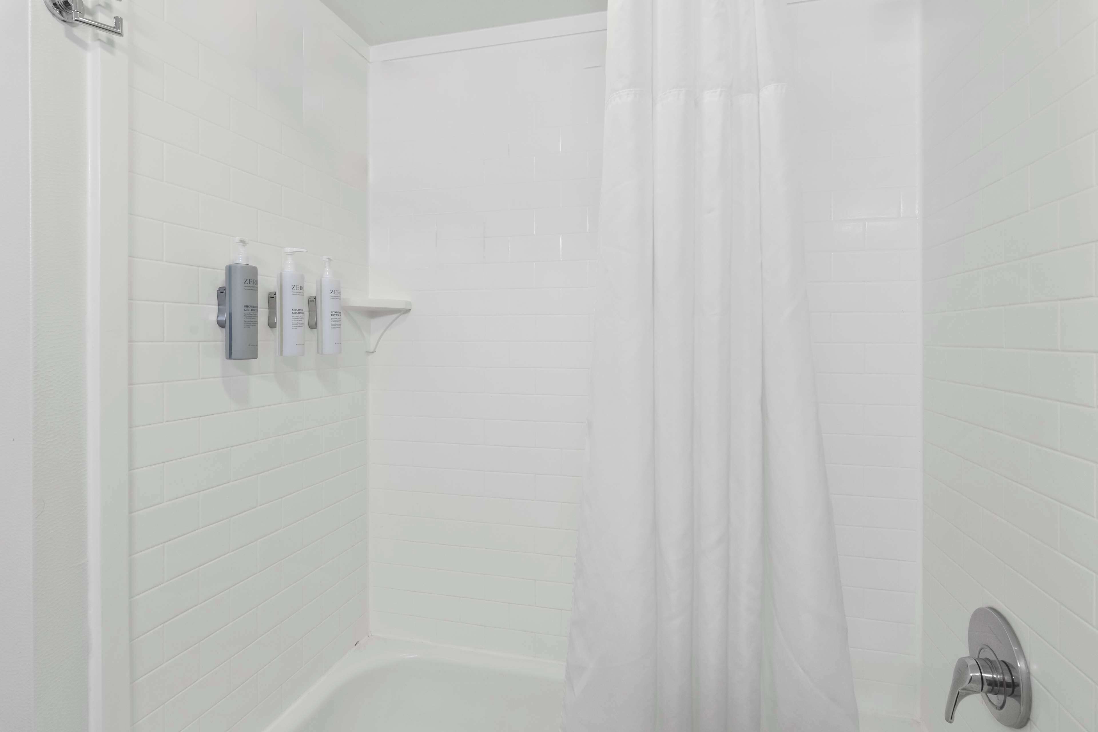 Un área de ducha con paredes de azulejos blancos, una cortina de baño y un grifo empotrado.