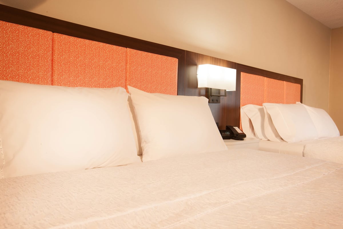 A hotel room with a large bed, a nightstand, and a wall-mounted lamp.