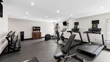 Un gimnasio con cintas de correr, una bicicleta estática y una banca.