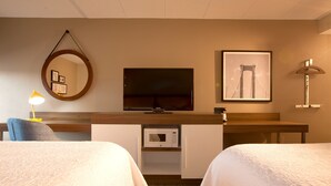 Habitación de hotel con dos camas, televisión, microondas, escritorio, silla, lámpara y un cuadro en la pared.