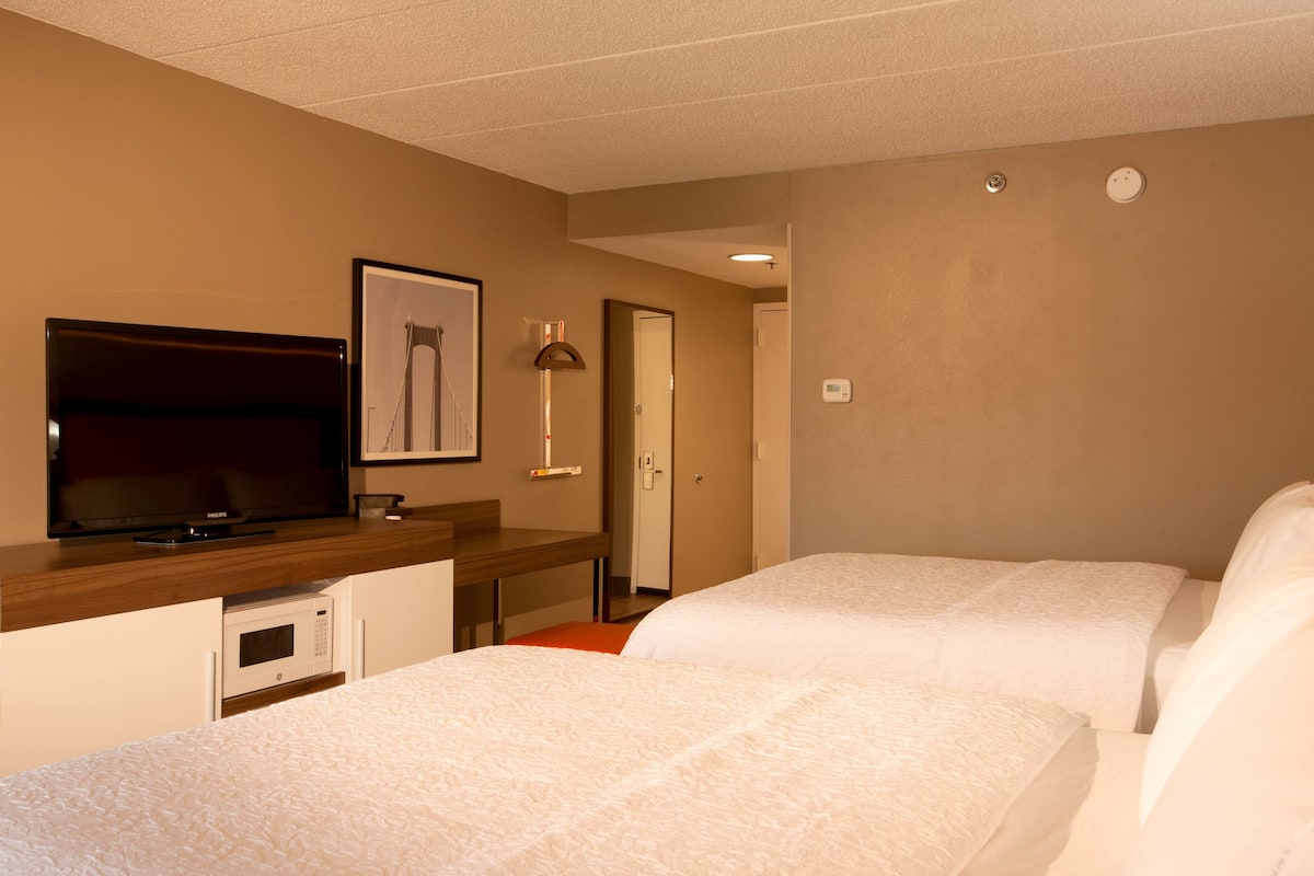 A hotel room with two beds, a television, a desk with a microwave, and a door leading to another room.