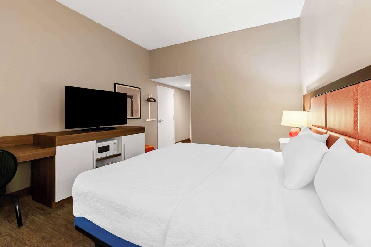 A hotel room with a bed, a desk with a television, a microwave, and a door leading to another room.