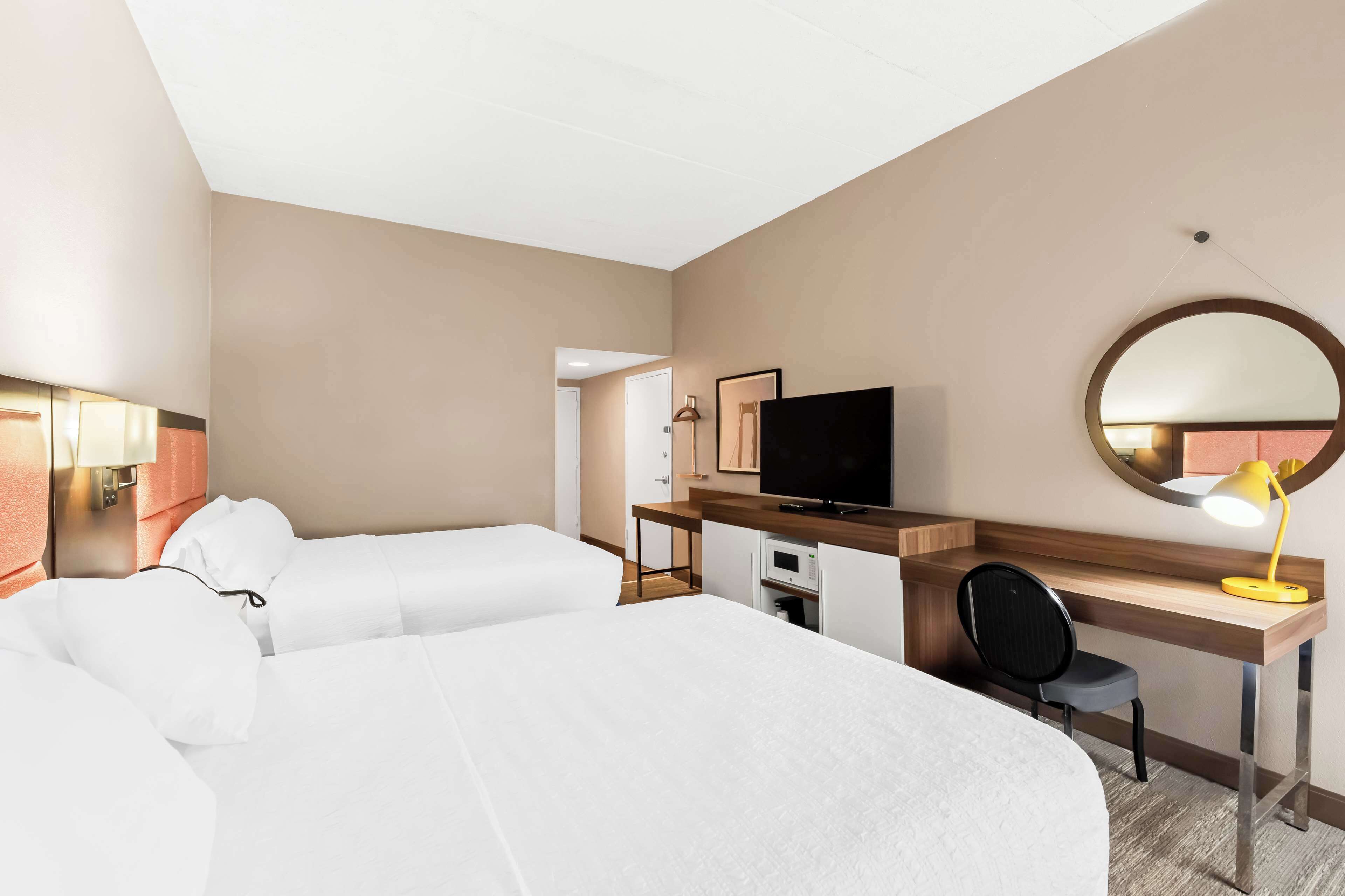 A hotel room with a large bed, a desk with a chair, a television, and a desk lamp.
