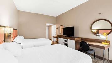 A hotel room with a large bed, a desk with a chair, a television, and a desk lamp.