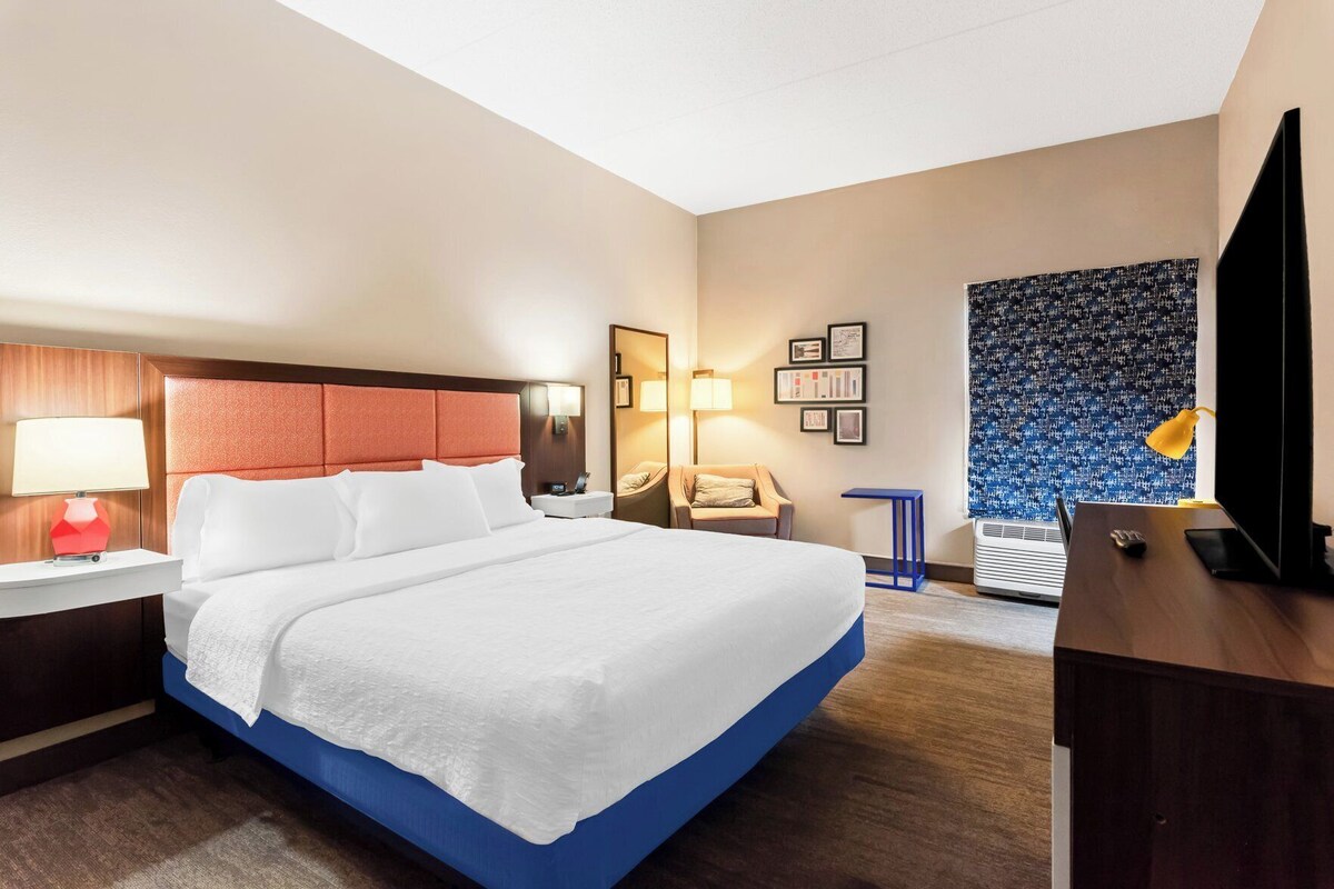 A hotel room with a bed, bedside tables, a desk, a TV, and a wall with framed pictures.