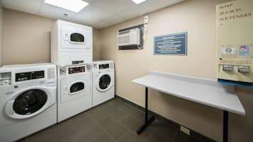 A laundry area with stacked washers and dryers, a coin-operated soap and bleach softener dispenser, and a guest laundry sign.