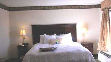 A hotel room with a large bed, two bedside tables, a nightstand, a lamp, a tray, and a window with curtains.