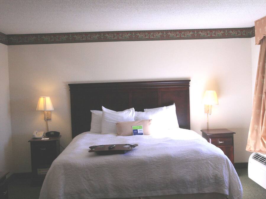 A hotel room with a large bed, two bedside tables, a nightstand, a lamp, a tray, and a window with curtains.