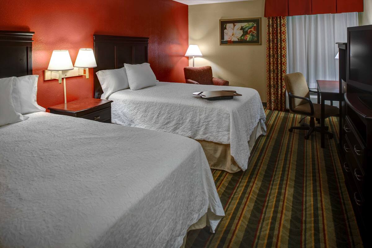 A hotel room with two beds, a TV, a desk, and a chair.