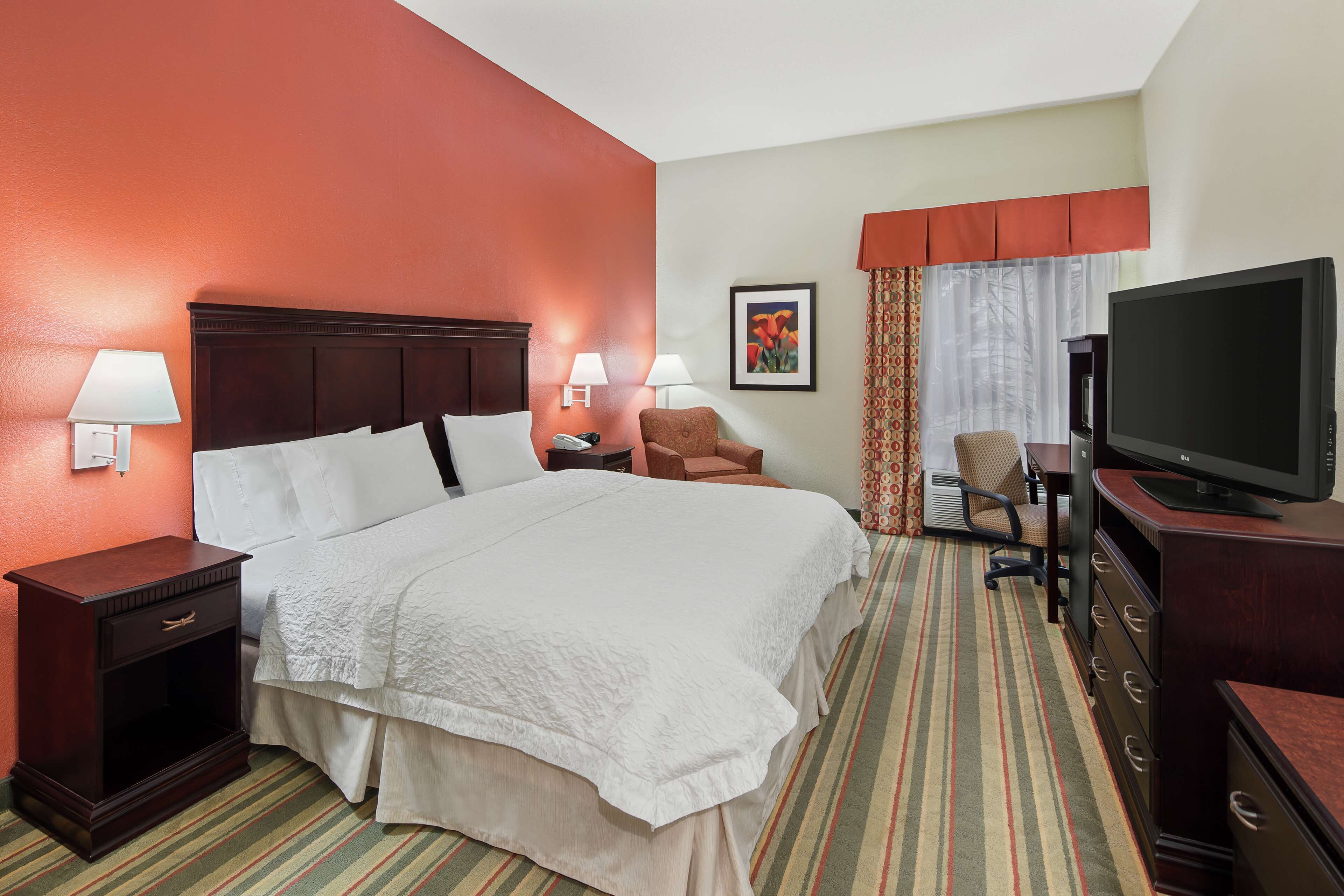 A hotel room with a large bed, a TV, a desk, and a chair.