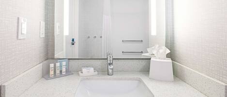 A modern bathroom with a large sink, a mirror, a shower, and a towel rack.