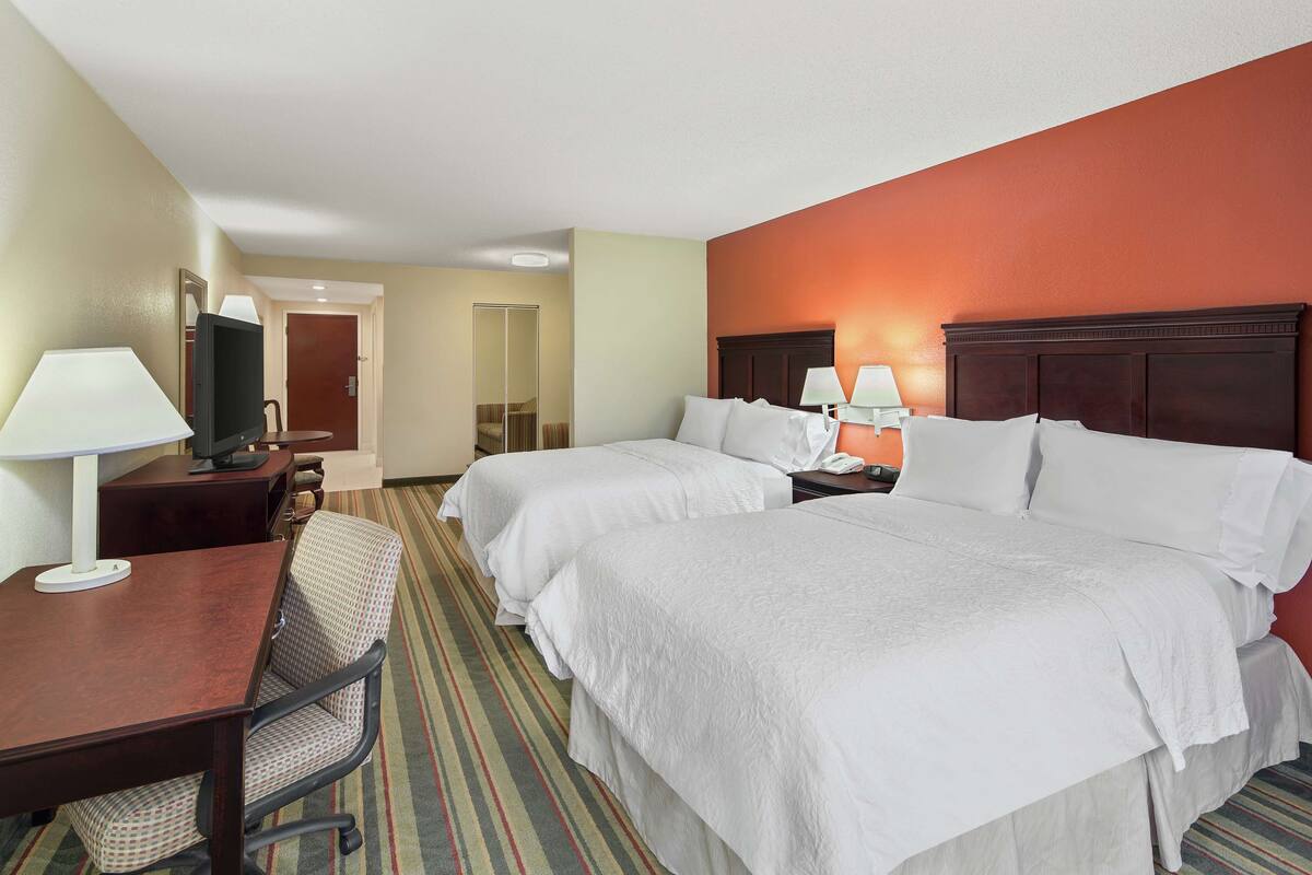 A hotel room with two beds, a desk, a chair, a TV, and a mirror.