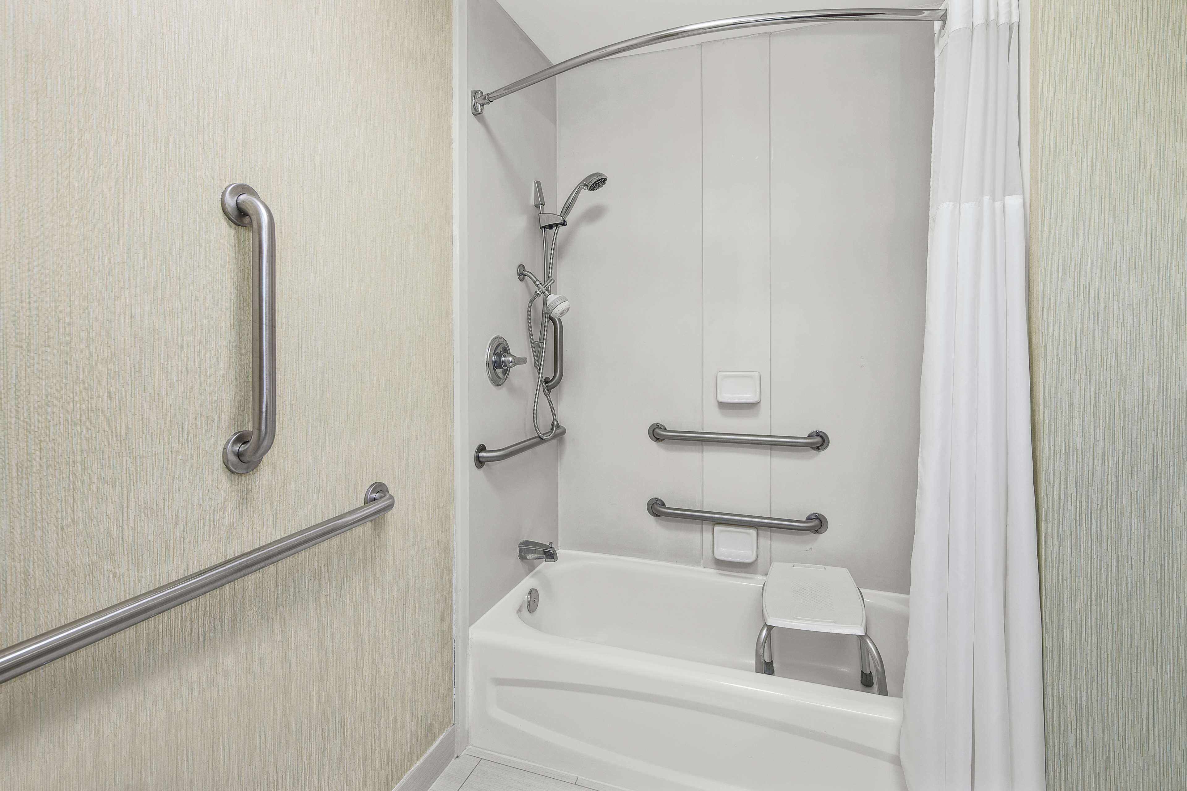 A bathroom with a bathtub, grab bars, a showerhead, and a towel rack.
