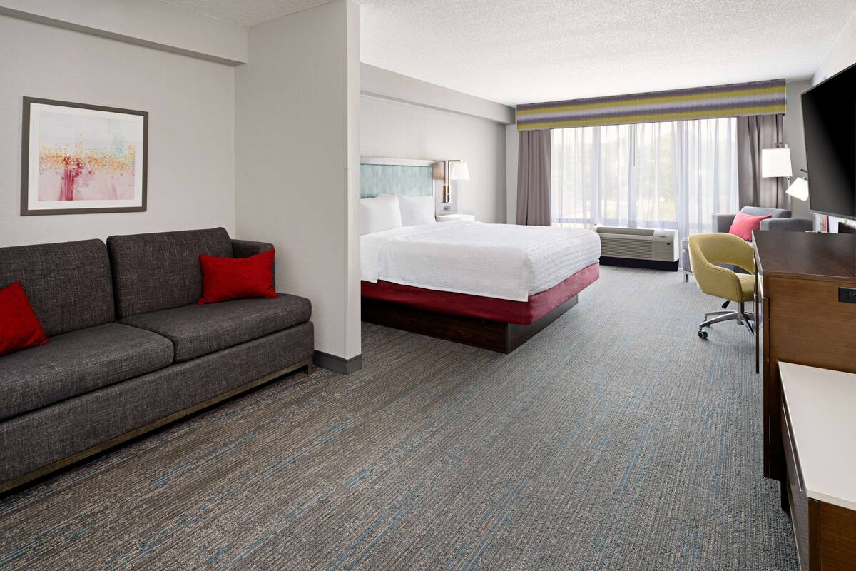 A hotel room with a bed, a sofa, a desk, and a TV.
