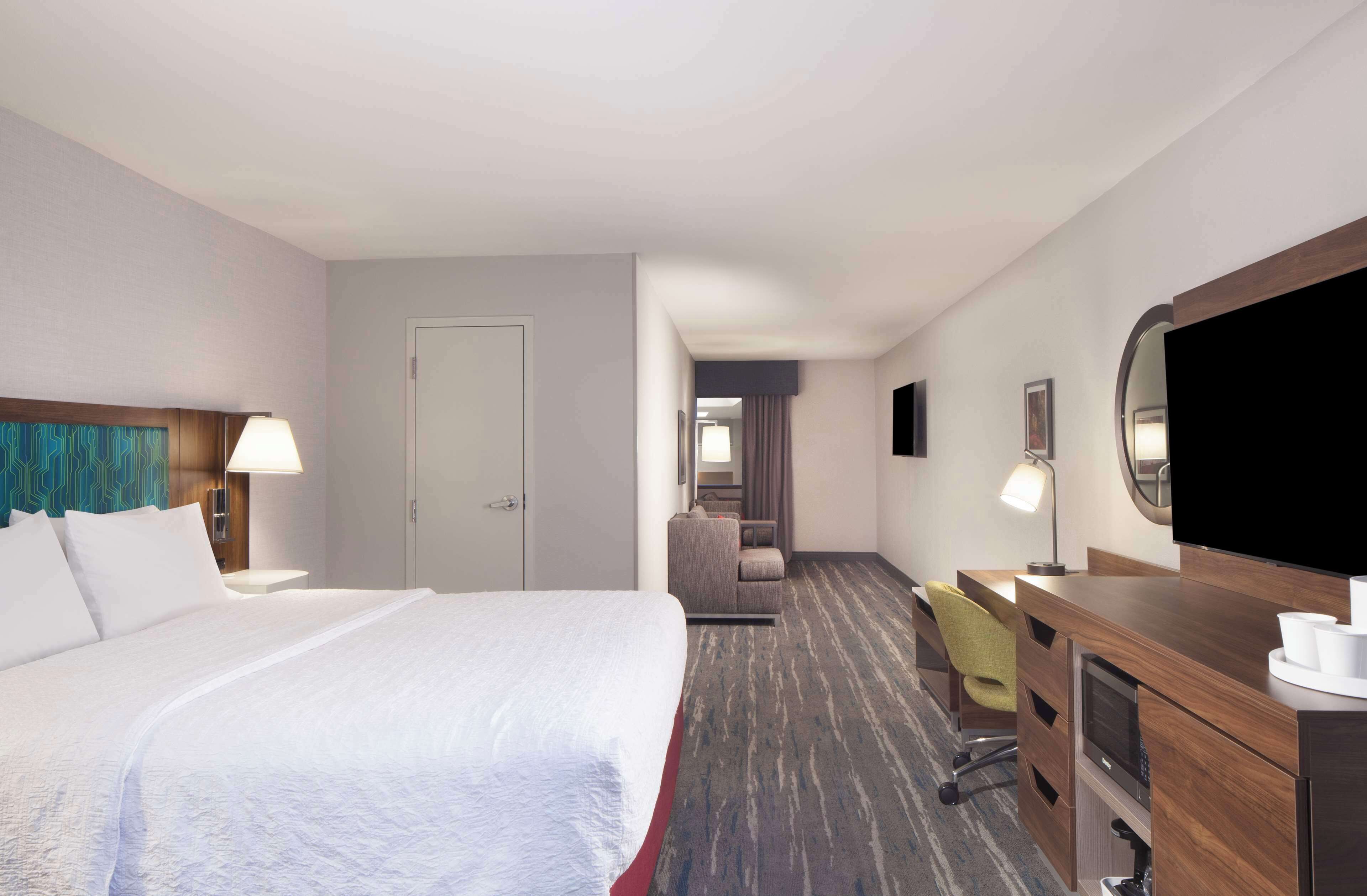 Una habitación de hotel con una cama grande, un escritorio con una silla, televisión y un armario.