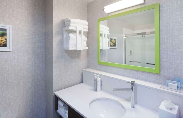 A modern bathroom with a white sink, a green-framed mirror, and neatly folded towels on a wall-mounted rack. - Hampton Inn Athens (Athens)
