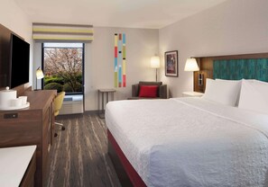 A hotel room with a bed, desk, chair, TV, and a view of a tree through a window.