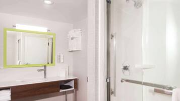 Un baño moderno con mampara de vidrio, un lavabo blanco con tocador de madera y un espejo con marco verde.