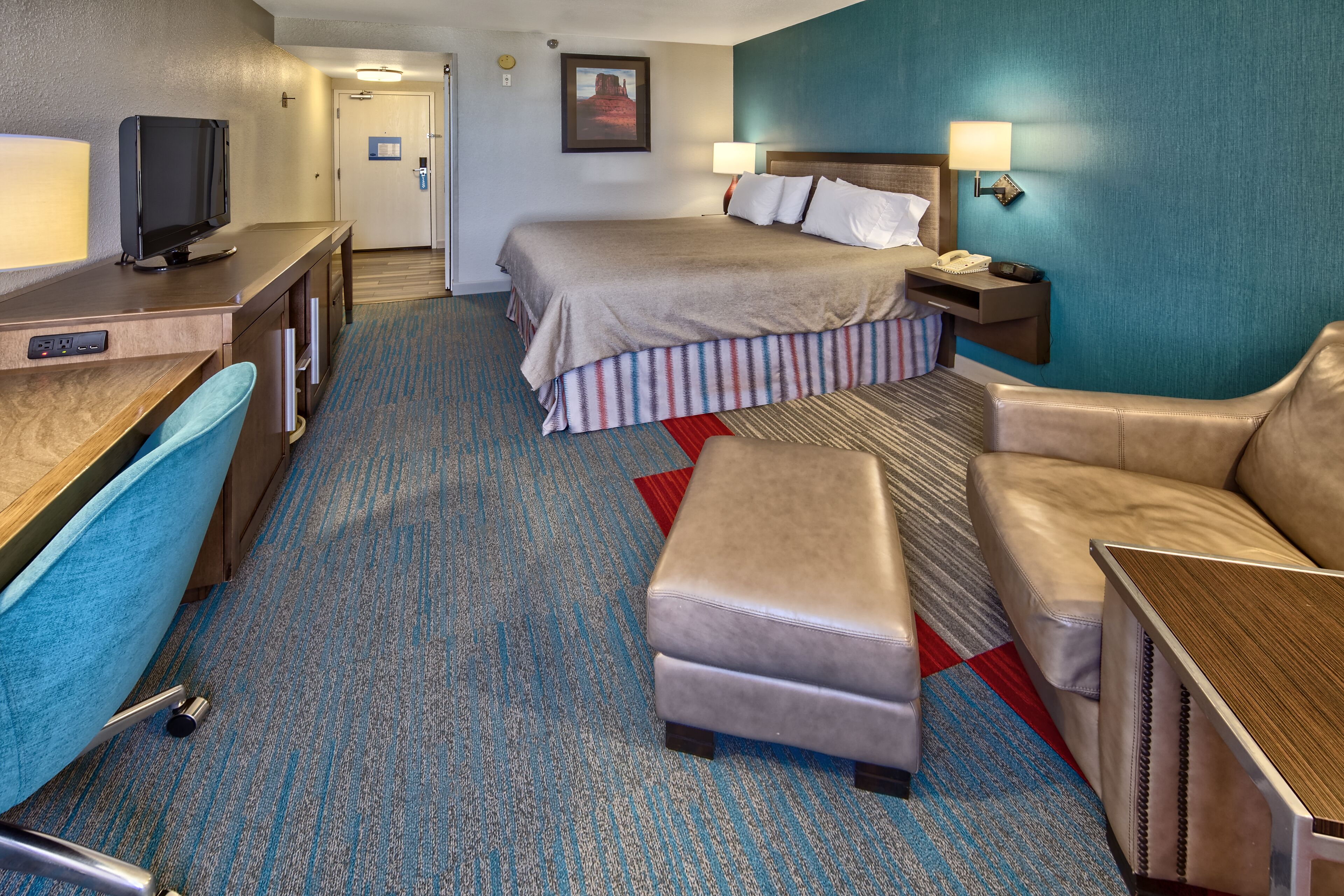 A hotel room with a bed, a desk with a television, a chair, a sofa, and a small table.