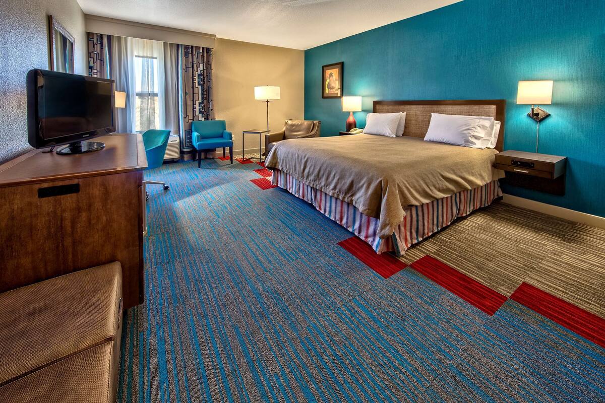 A hotel room with a large bed, a desk with a television, a chair, and a desk lamp.