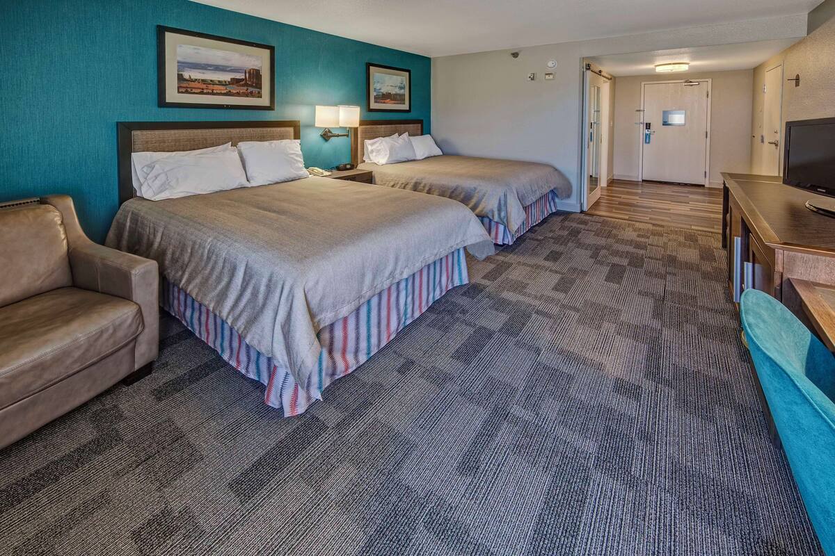 A hotel room with two beds, a sofa, a TV, and a desk.