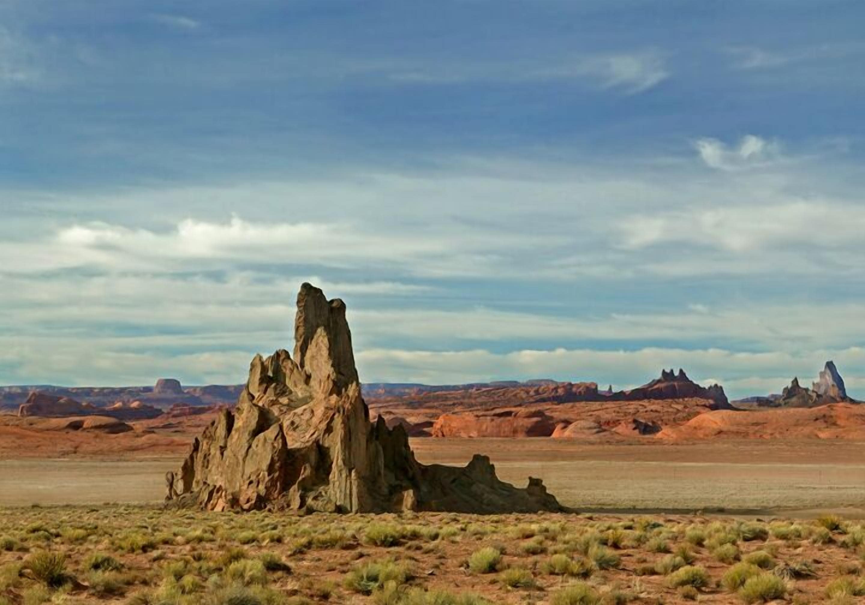 A rock formation in a desert landscape with distant hills.