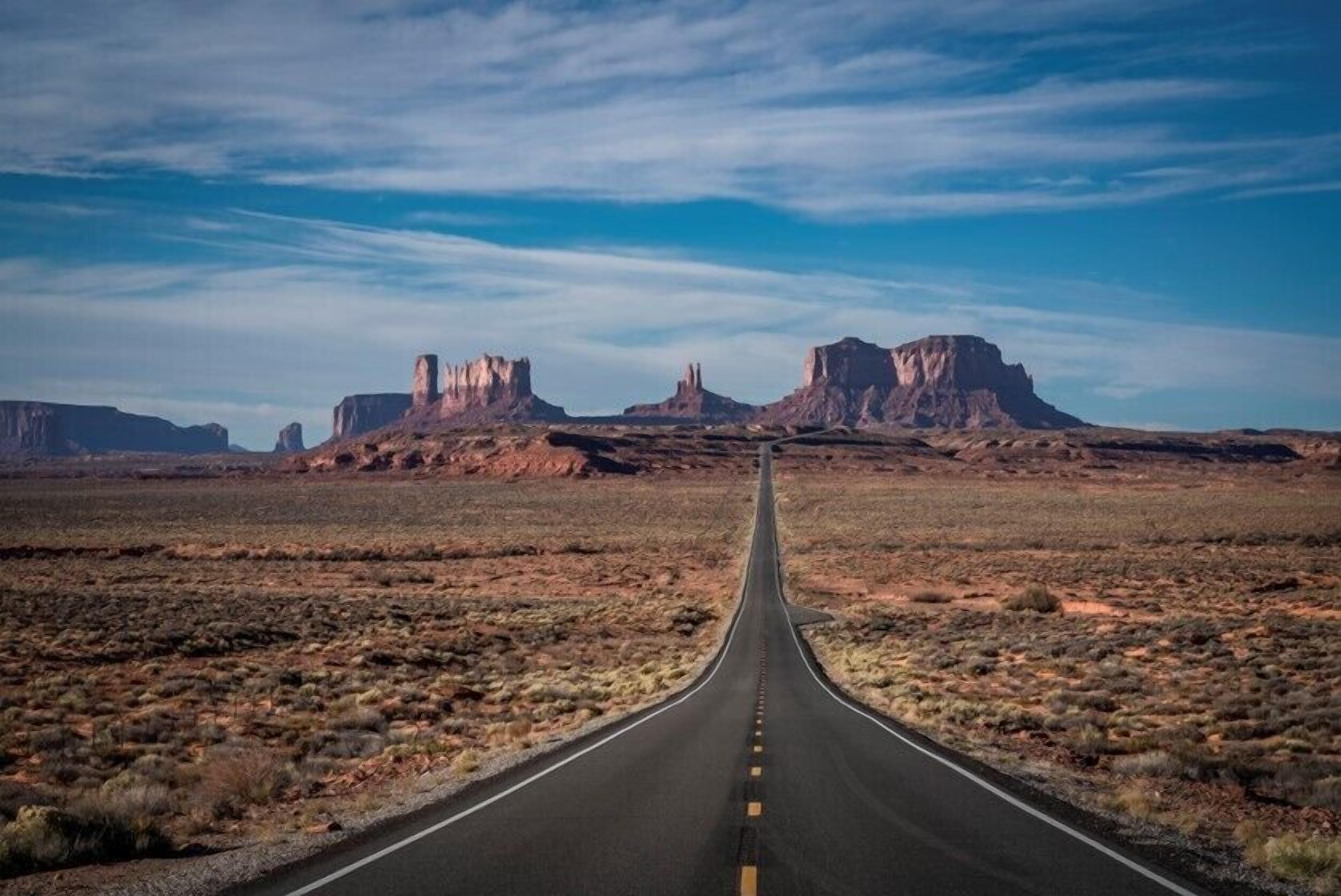 Eine gerade Straße führt durch eine Wüstenlandschaft mit Felsformationen an beiden Seiten.