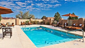 A pool area with lounge chairs and umbrellas, surrounded by walls and trees.
