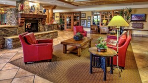 A spacious living area with a stone fireplace, red leather chairs, a wooden coffee table, and a television mounted on the wall.