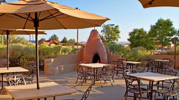 An outdoor patio with tables and chairs, a clay oven, and umbrellas.