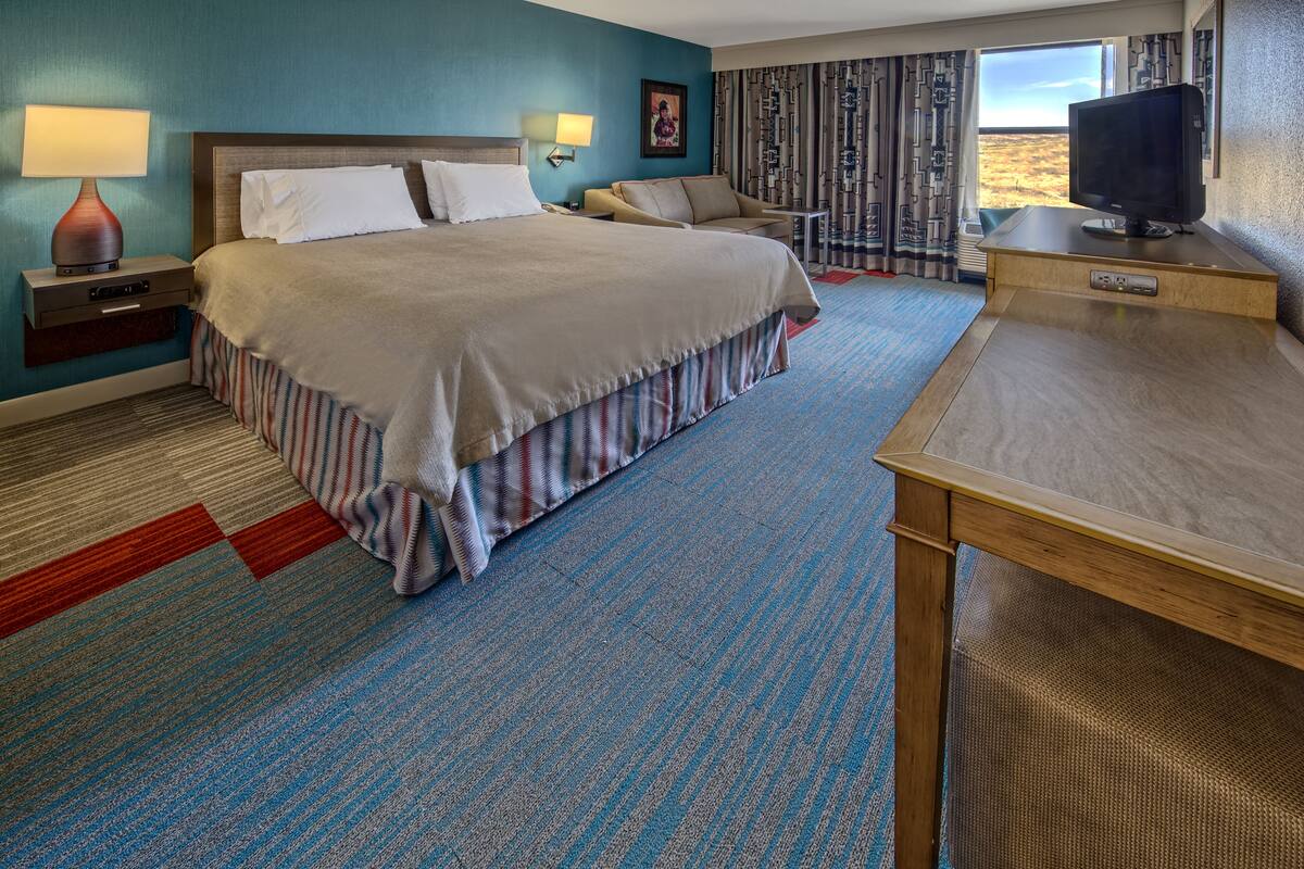A hotel room with a large bed, a desk with a computer, a TV, and a window with a view.