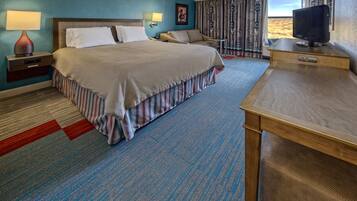A hotel room with a large bed, a desk with a computer, a TV, and a window with a view.