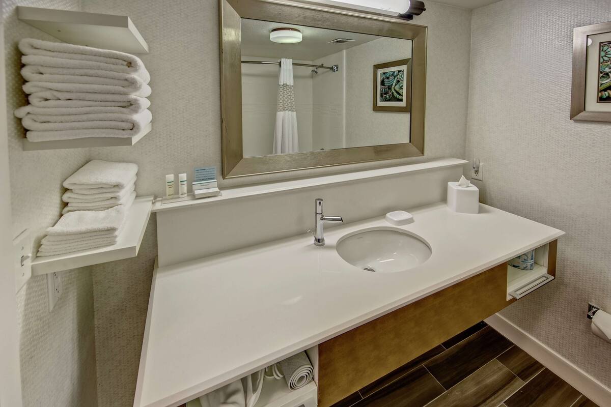 A modern bathroom with a white sink, a large mirror, and neatly folded towels on a shelf.