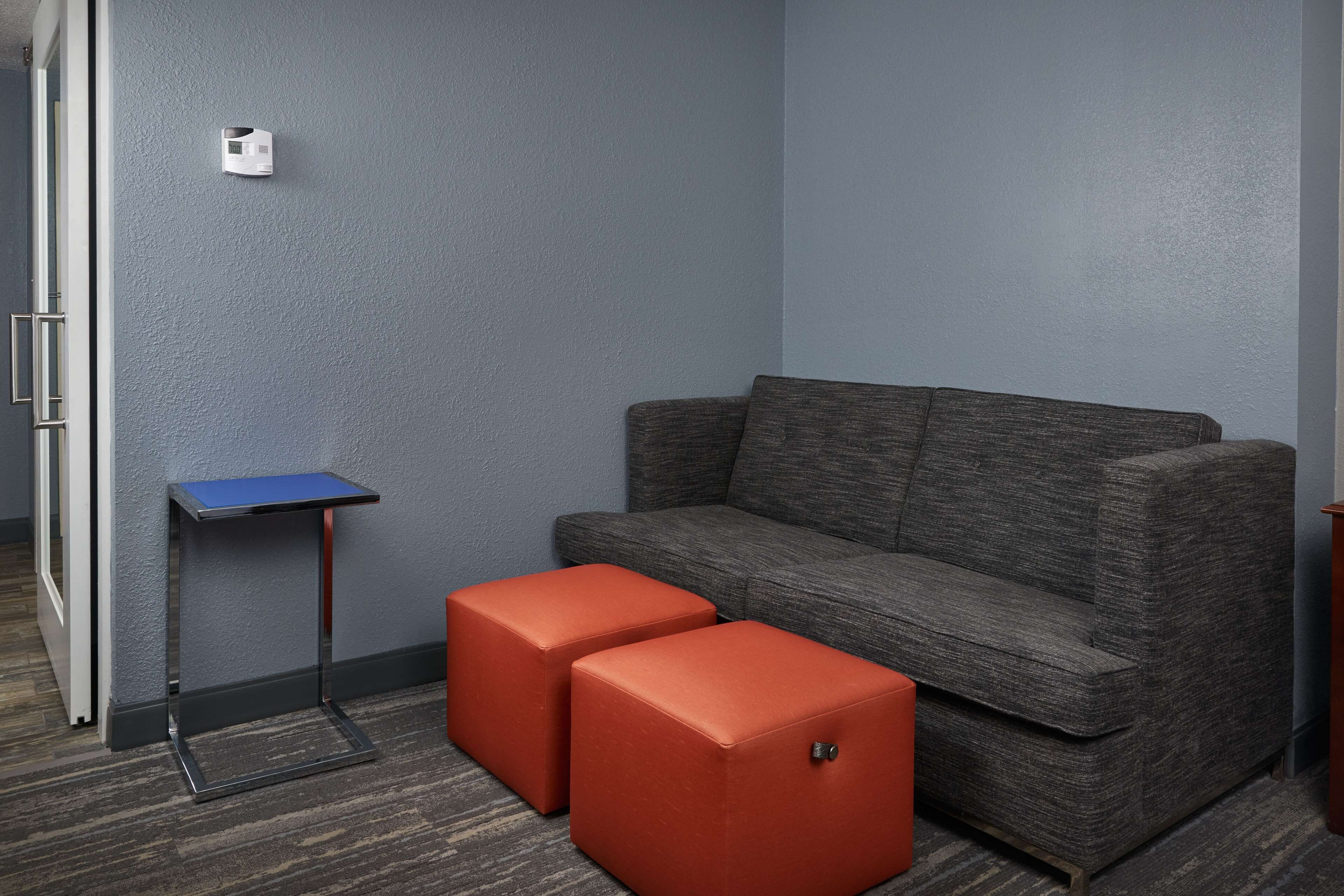 A room with a grey sofa, two red ottomans, a small blue table, and a wall-mounted light fixture.